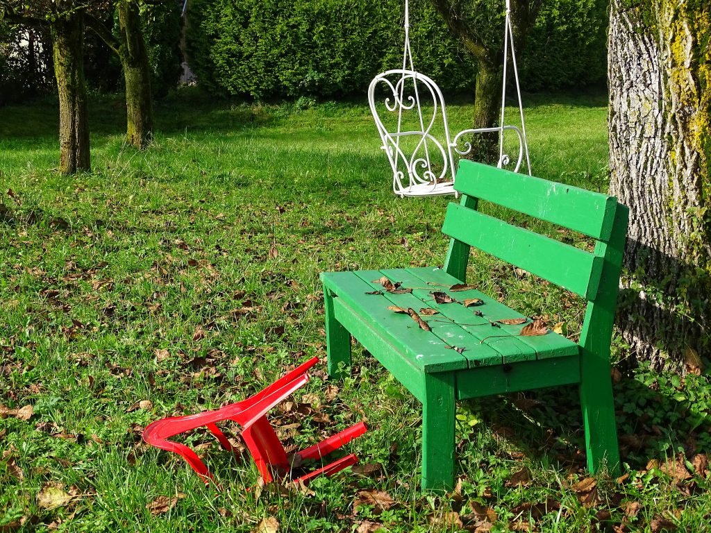 Eine grüne Bank steht neben einem Baum und ein roter Plastikstuhl liegt daneben