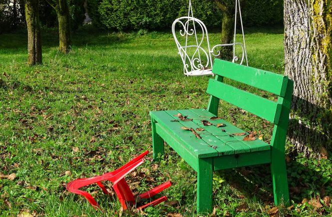 Eine grüne Bank steht neben einem Baum und ein roter Plastikstuhl liegt daneben