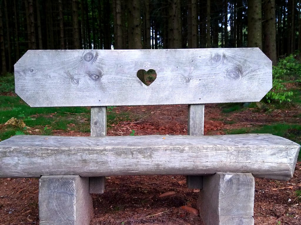 Ein graues, grob gezimmertes Bankerl beim Baumkronen-Weg in Kopfing. Es hat in der Mitte ein hübsches Herz.