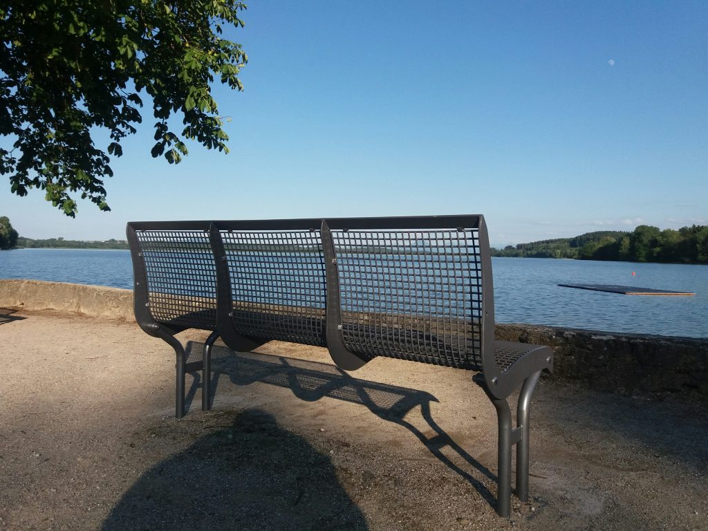 Eine Bank im Vordergrund und im Hintergrund der Waginger See vor einem wolkenlosen Himmel