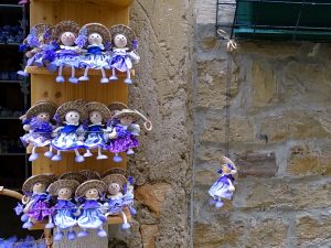 Kleine Puppen mit Strohhut und violettem Kleid auf einem Holzregal