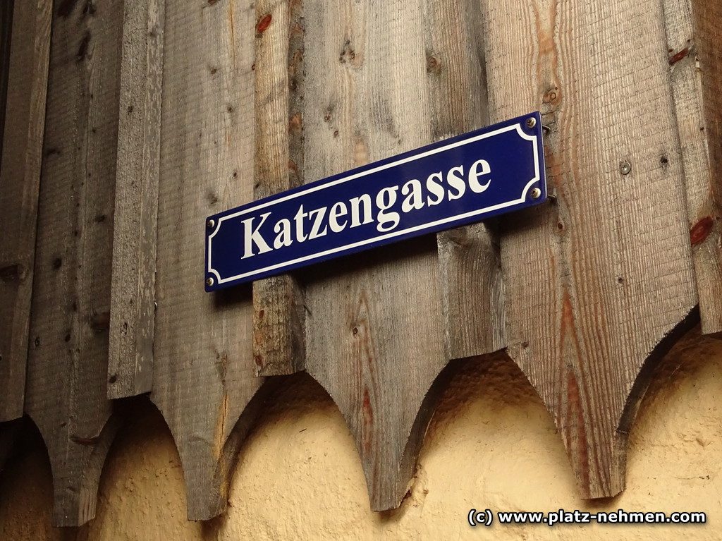 Eine Holzfassade auf der ein blaues Schild mit Katzengasse hängt